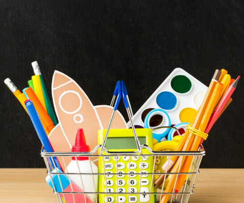 A wire basket filled with school supplies including pencils, markers, a calculator, and paint set